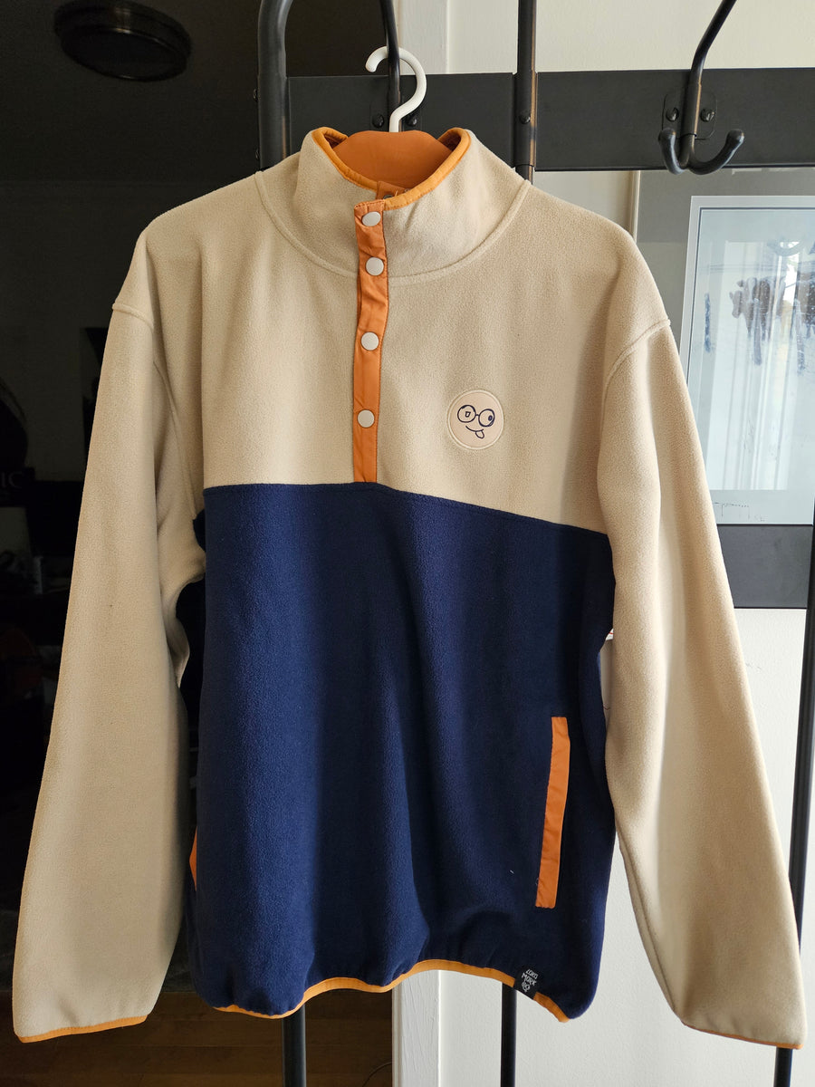 Front view of beige and navy colorblock fleece pullover on a hanger, showing orange snap placket and pocket trim