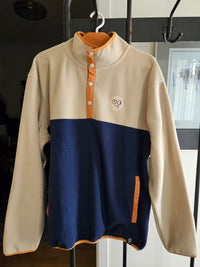 Front view of beige and navy colorblock fleece pullover on a hanger, showing orange snap placket and pocket trim