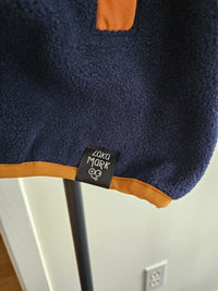 Close-up of navy fleece fabric with orange hem binding and a black Laka Mark label