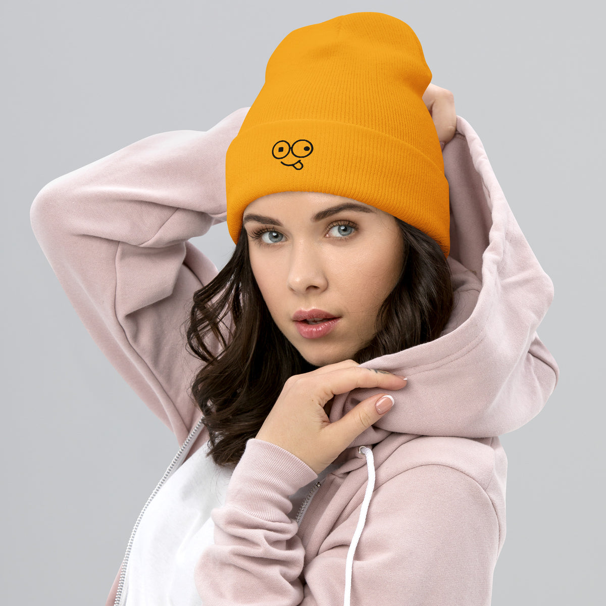 Model wearing a gold cuffed knit beanie with a black tongue-out glasses-face design