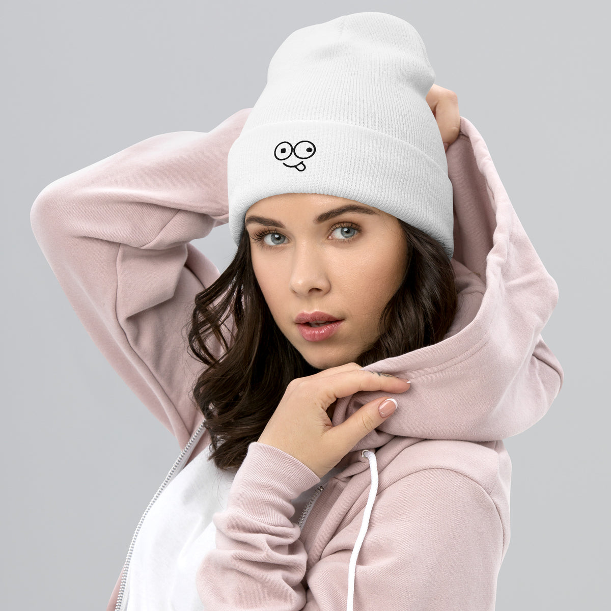 Model wearing a white cuffed knit beanie with a black tongue-out glasses-face design