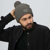 Model wearing a dark heather grey pom-pom knit beanie with a folded cuff and white tongue-out glasses-face design