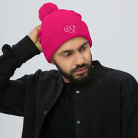 Model wearing a neon pink pom-pom knit beanie with a folded cuff and white tongue-out glasses-face design