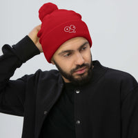 Model wearing a red pom-pom knit beanie with a folded cuff and light-colored tongue-out glasses-face design