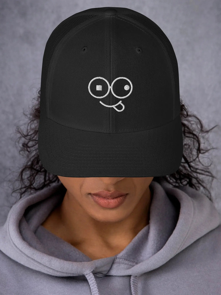Model wearing a black trucker hat with a curved brim and white tongue-out glasses-face design