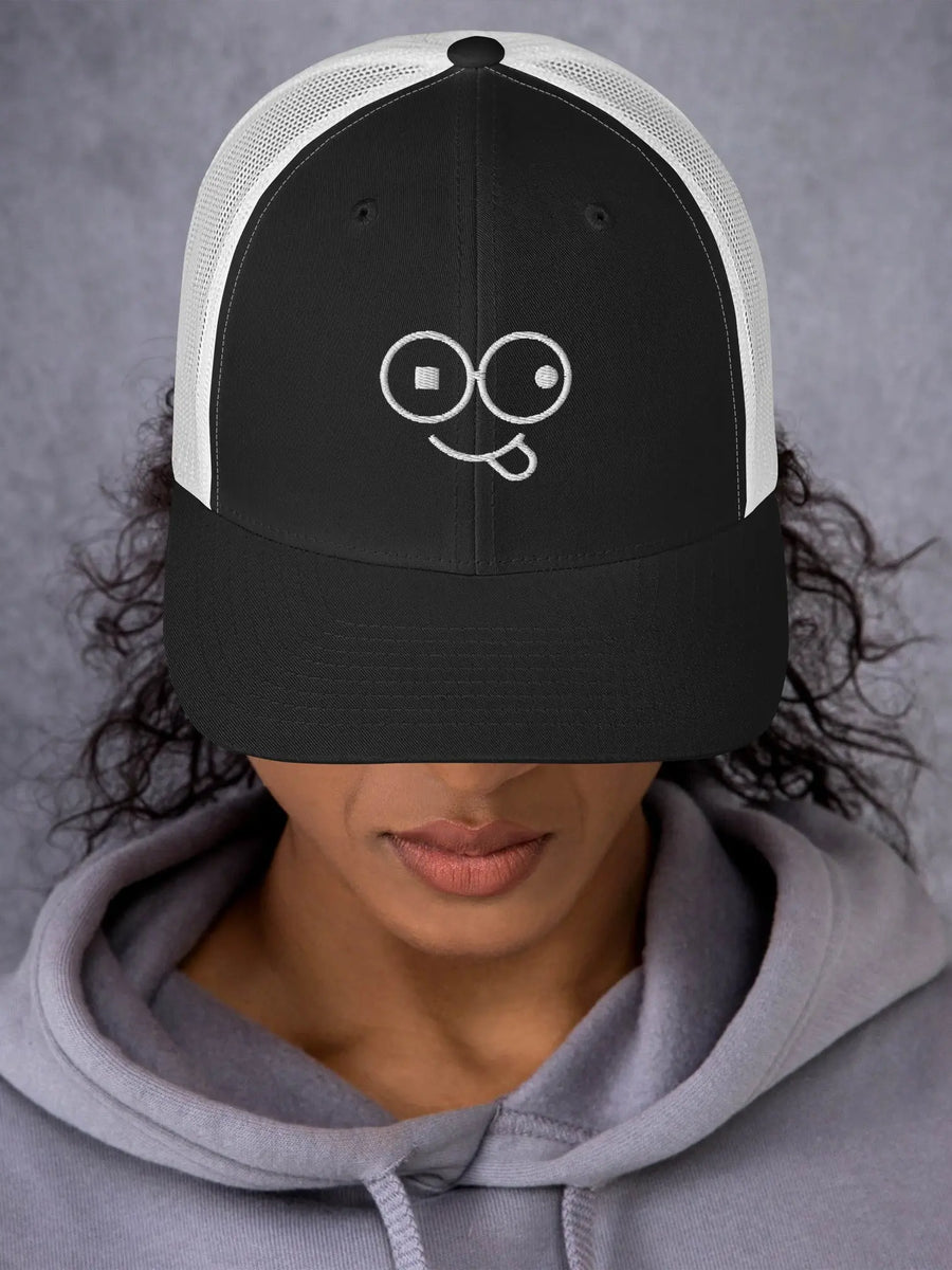 Model wearing a black trucker hat with white mesh panels and a white tongue-out glasses-face design