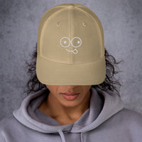 Model wearing a khaki trucker hat with a curved brim and white tongue-out glasses-face design