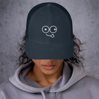 Model wearing a navy trucker hat with a curved brim and white tongue-out glasses-face design