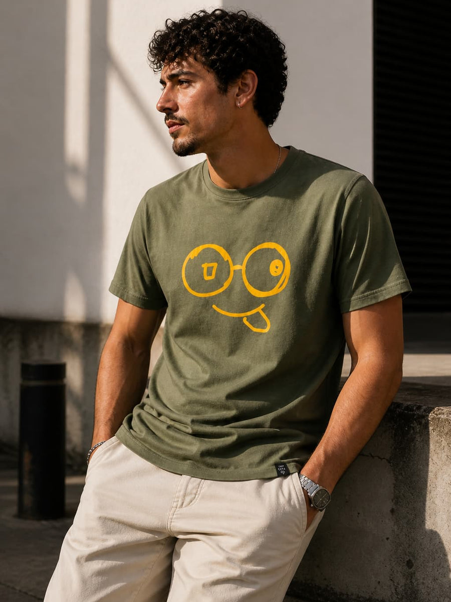Model wearing a green short sleeve t-shirt with a large yellow glasses-face graphic and tongue-out smile