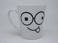 Close-up of white coffee mug with black round glasses, mismatched eyes and a tongue-out smile against a light background