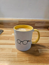 White ceramic mug with yellow interior and handle, glasses illustration, and a drink on a wooden countertop