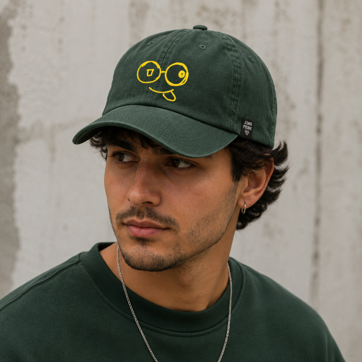 Model wearing a washed green dad hat with a yellow glasses-face logo and curved brim