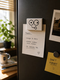 White rectangular smiley face fridge magnet with black glasses design holding a handwritten reminder on a dark refrigerator