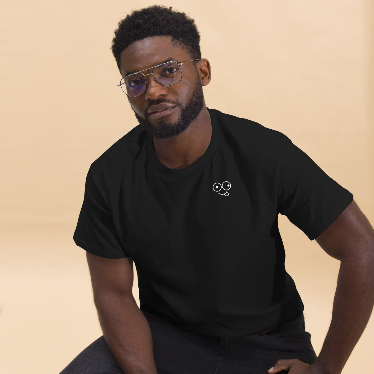 Close-up of a model wearing a black crew neck t-shirt with a white tongue-out glasses-face chest design