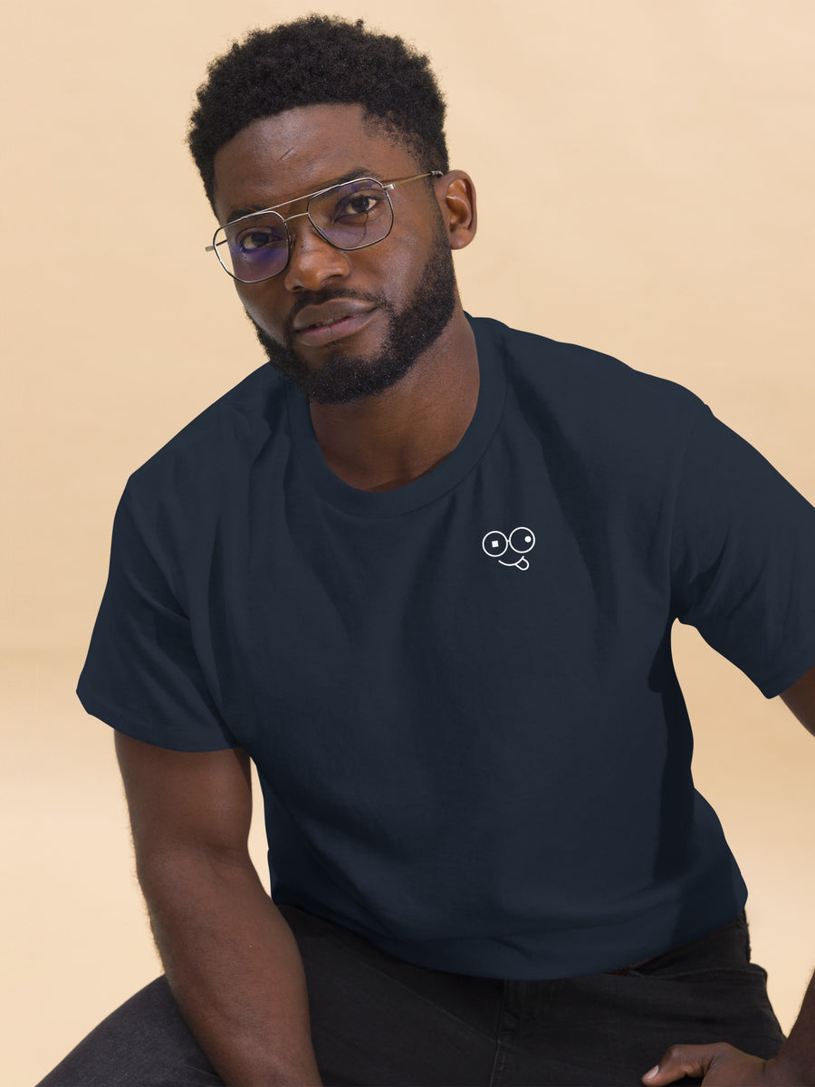 Seated model wearing a navy crew neck t-shirt with a small white tongue-out glasses-face chest design