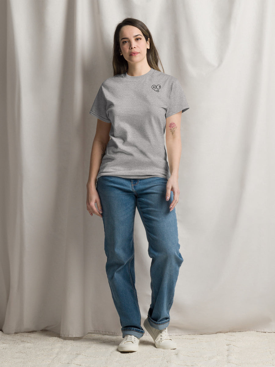 Model wearing a sport grey crew neck t-shirt with a small black glasses-face chest design and blue jeans