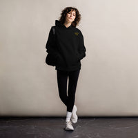 Model wearing a black oversized pullover hoodie with a small yellow glasses-face chest design and front kangaroo pocket