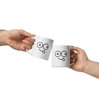 Two white mugs held together in a toast, each featuring black round glasses, mismatched eyes and a tongue-out smile