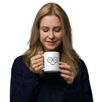Person holding a white mug with a smiling glasses-face design and closed eyes, with the handle on the left
