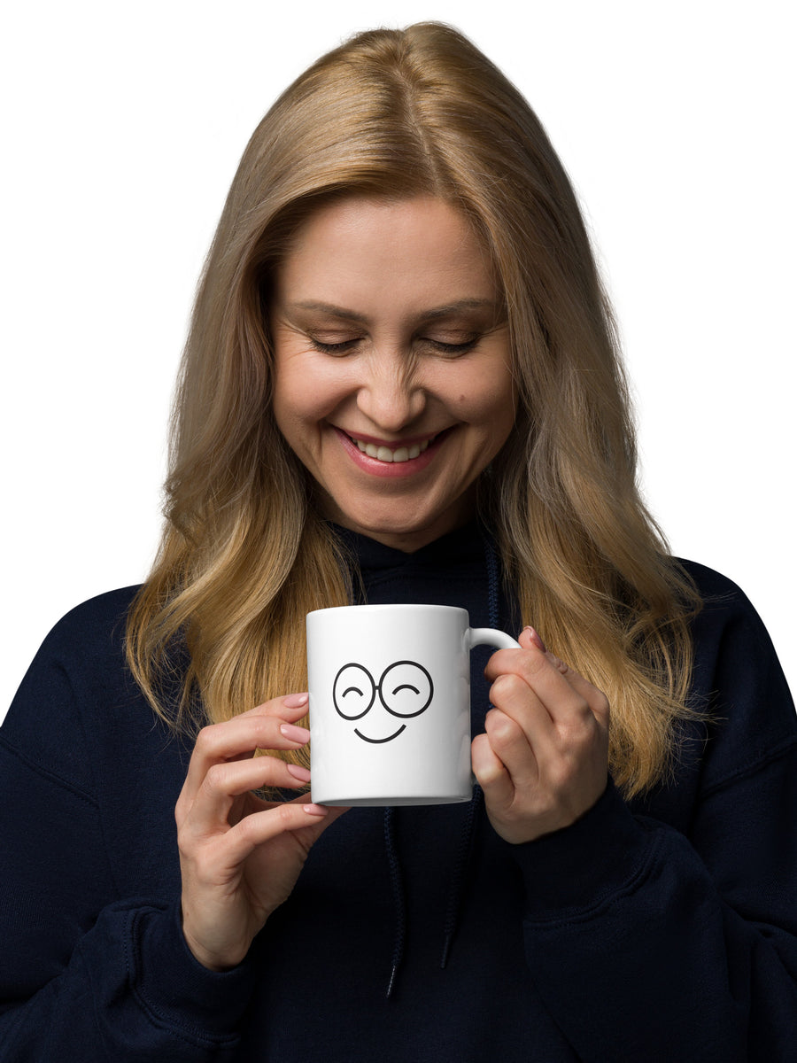 Person holding a white smiling-face mug near their chin, showing black round glasses and a left-side handle