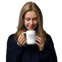 Person looking down at a white mug with black smiling glasses-face artwork and a right-side handle
